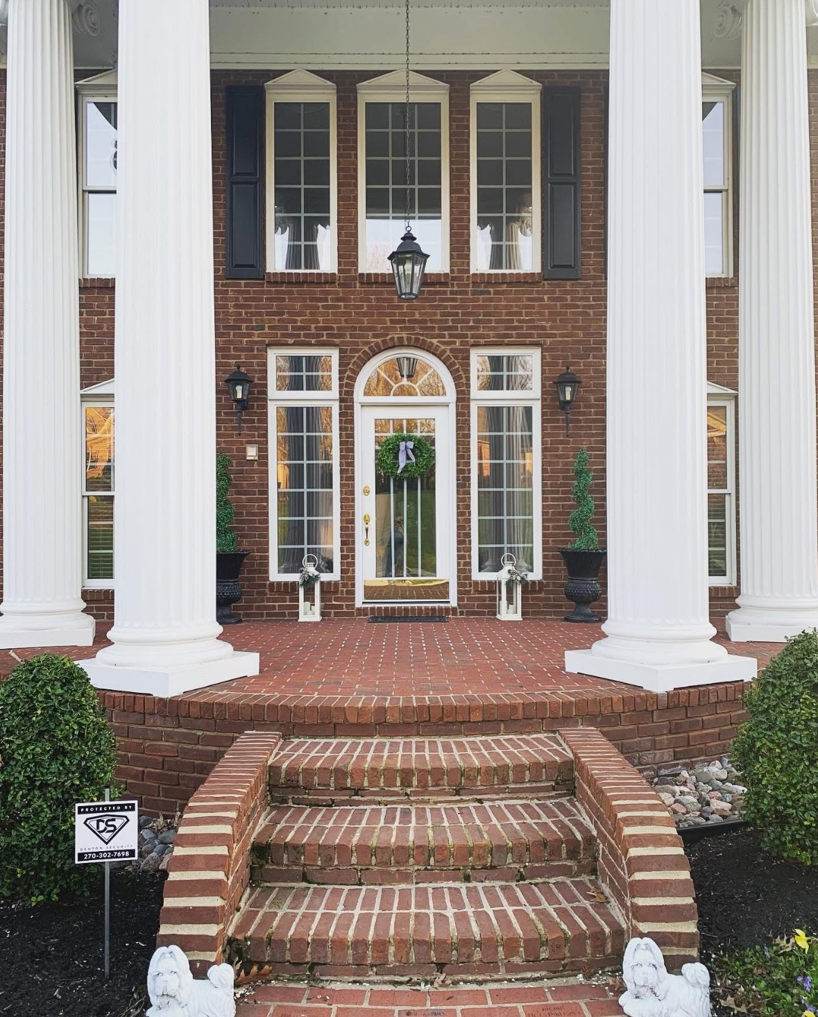 Two-story brick home with white columns, protected by a Denton Security yard sign at the front steps